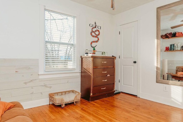 sitting room featuring ceiling fan, wood walls, a wealth of natural light, and light hardwood / wood-style flooring