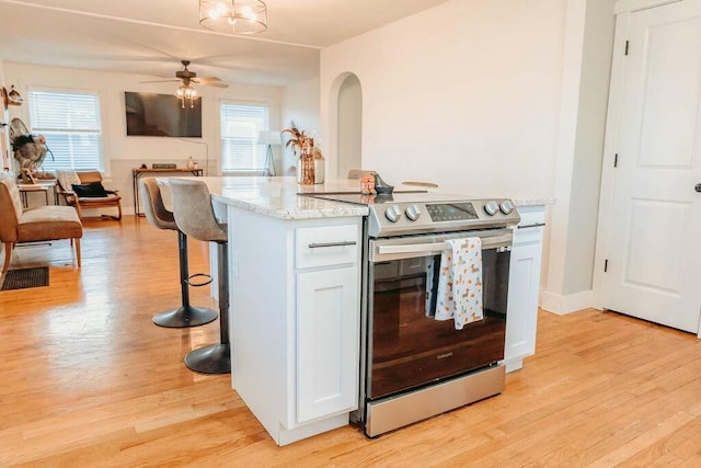 kitchen with light wood-type flooring, ceiling fan, white cabinets, a breakfast bar area, and stainless steel electric range