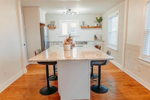 kitchen featuring a kitchen bar, light stone countertops, white refrigerator, white cabinets, and a kitchen island