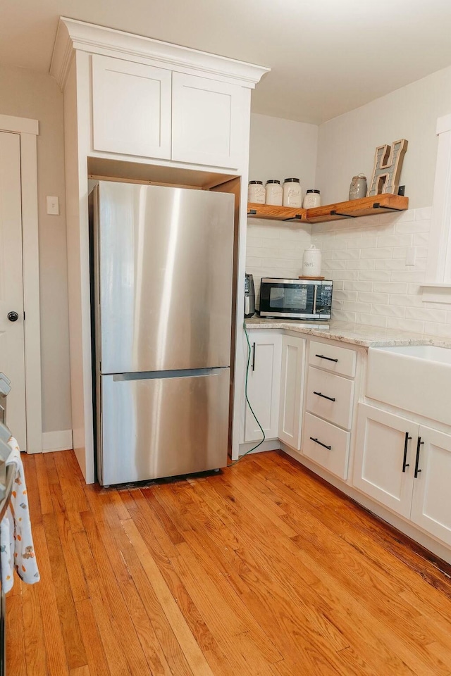 kitchen featuring tasteful backsplash, white cabinets, light wood-type flooring, and appliances with stainless steel finishes