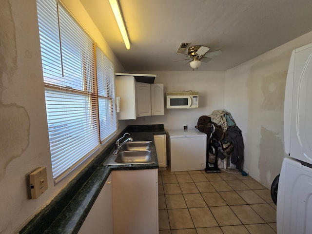 kitchen with sink, ceiling fan, light tile patterned floors, stacked washer / drying machine, and white cabinetry