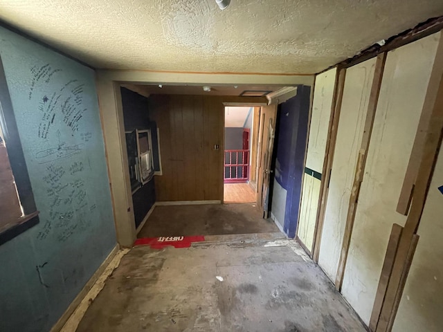 hallway with a textured ceiling, concrete floors, and wood walls