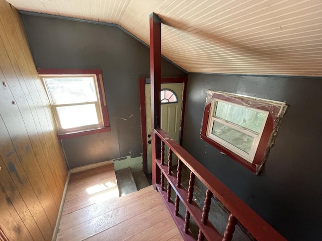 hall with wooden walls, hardwood / wood-style flooring, vaulted ceiling, and wooden ceiling