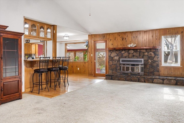 kitchen featuring wooden walls, vaulted ceiling, light colored carpet, kitchen peninsula, and a breakfast bar area