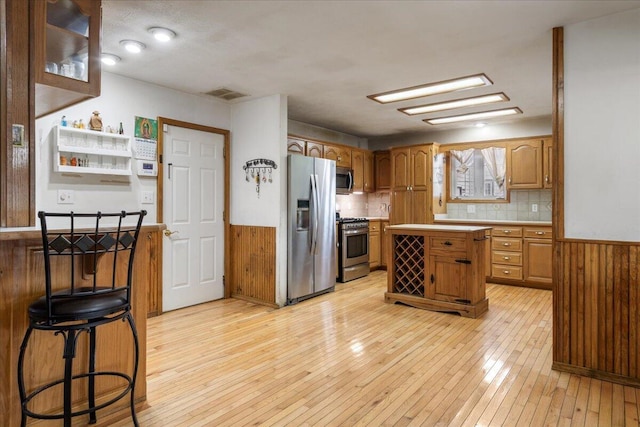 kitchen with stainless steel appliances, light hardwood / wood-style flooring, a kitchen bar, wooden walls, and a kitchen island