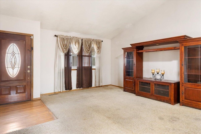 foyer featuring a healthy amount of sunlight, light colored carpet, and lofted ceiling