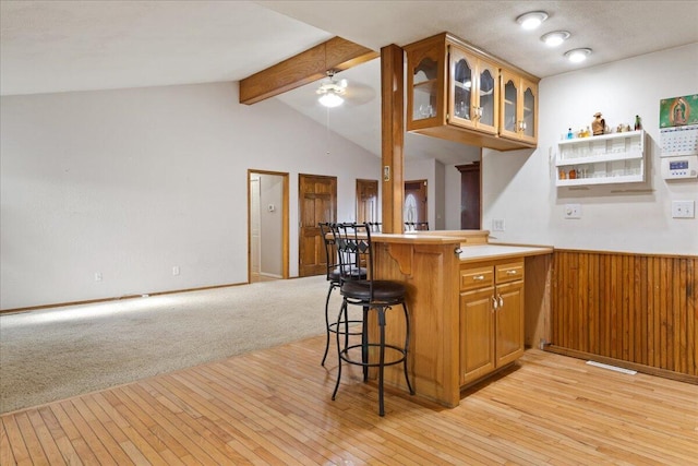 kitchen featuring kitchen peninsula, light colored carpet, ceiling fan, vaulted ceiling with beams, and a breakfast bar area