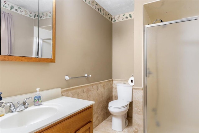 bathroom with vanity, a shower with door, toilet, and tile walls