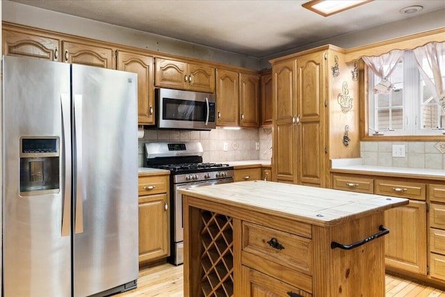 kitchen featuring light hardwood / wood-style flooring, appliances with stainless steel finishes, tasteful backsplash, tile counters, and a kitchen island