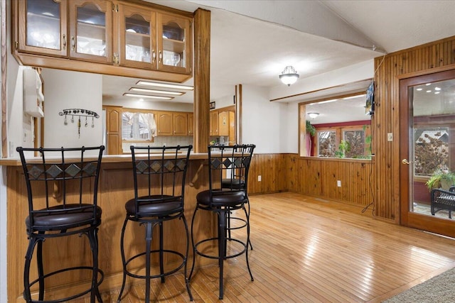 interior space featuring wood walls, light wood-type flooring, a breakfast bar area, and vaulted ceiling