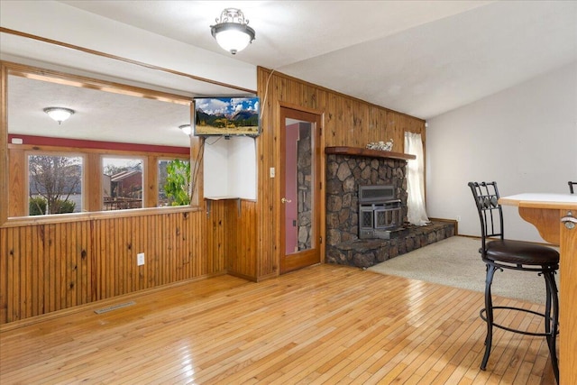 interior space with a wood stove, wooden walls, light hardwood / wood-style floors, and lofted ceiling