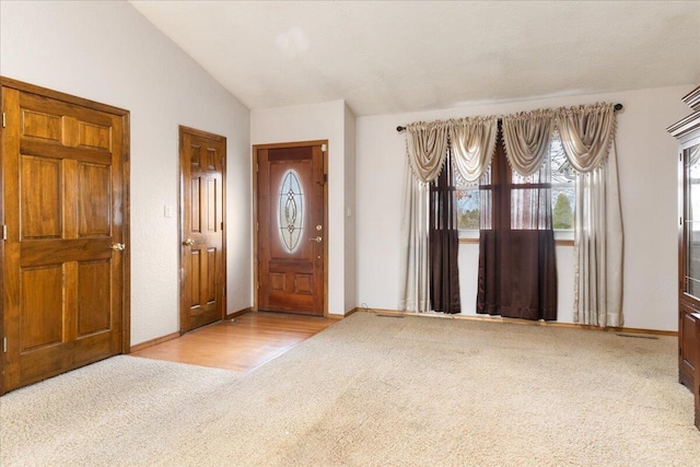 foyer entrance with light colored carpet and vaulted ceiling