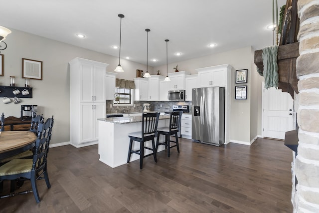 kitchen with appliances with stainless steel finishes, light stone counters, white cabinets, a center island, and hanging light fixtures