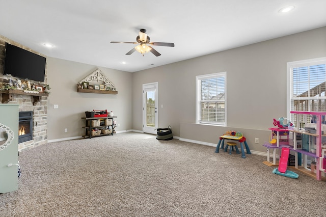 rec room with carpet floors, a stone fireplace, and ceiling fan