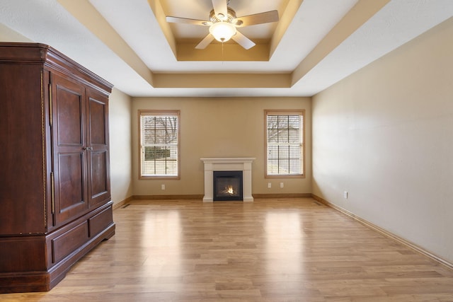 unfurnished living room featuring a raised ceiling, a wealth of natural light, ceiling fan, and light wood-type flooring