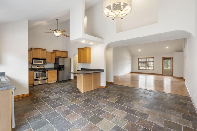 kitchen with a high ceiling, kitchen peninsula, a breakfast bar area, ceiling fan with notable chandelier, and appliances with stainless steel finishes