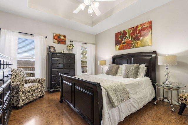 bedroom with ceiling fan, dark hardwood / wood-style flooring, and a tray ceiling