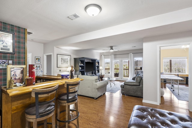 living room featuring a textured ceiling, indoor bar, hardwood / wood-style flooring, and ceiling fan