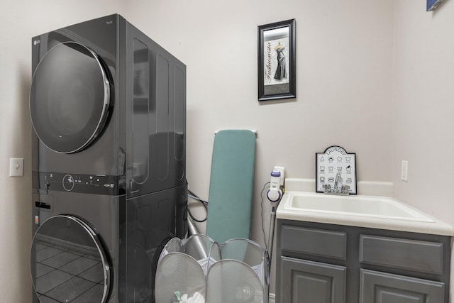 clothes washing area with tile patterned floors, stacked washer and dryer, cabinets, and sink