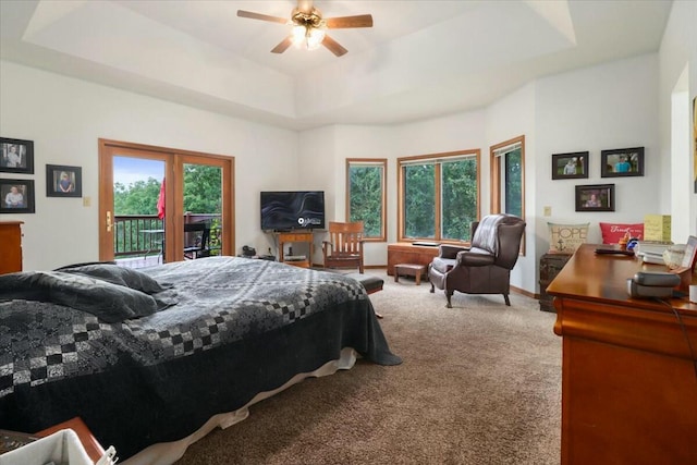 carpeted bedroom featuring ceiling fan, access to exterior, and a tray ceiling