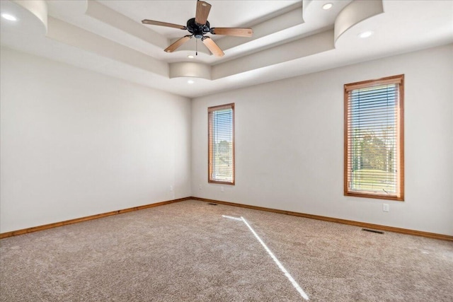 carpeted spare room featuring a raised ceiling and ceiling fan