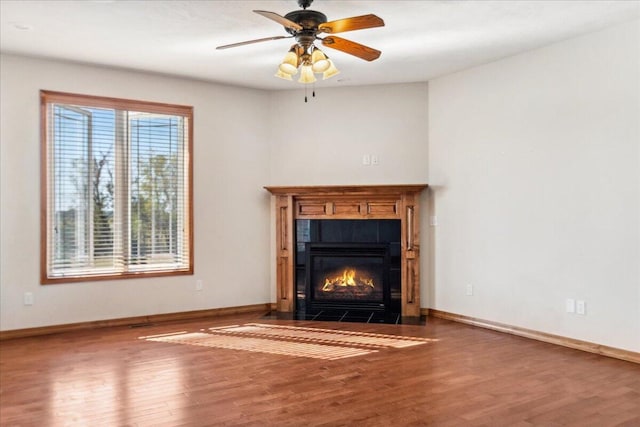 unfurnished living room with ceiling fan, wood-type flooring, and a tile fireplace