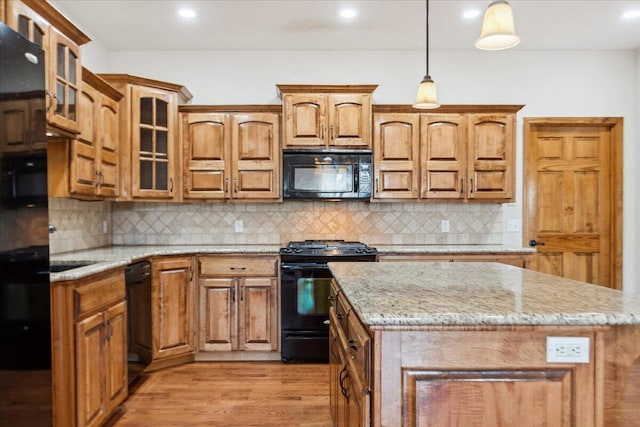 kitchen with pendant lighting, a center island, black appliances, light stone countertops, and light hardwood / wood-style flooring