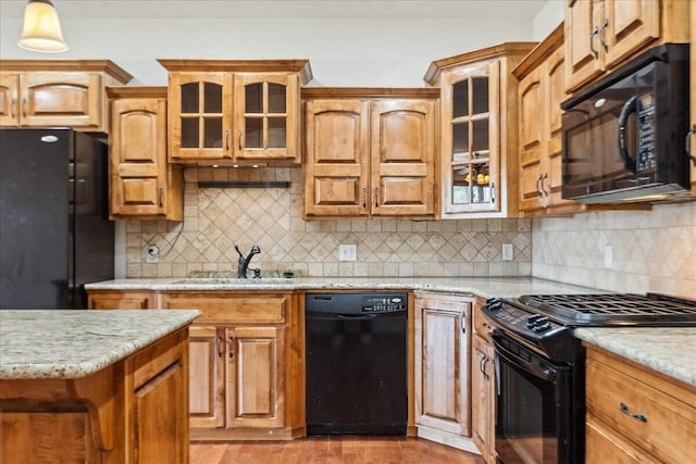 kitchen with pendant lighting, sink, backsplash, light stone counters, and black appliances