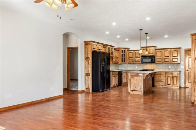 kitchen with backsplash, wood-type flooring, black appliances, a kitchen island, and decorative light fixtures