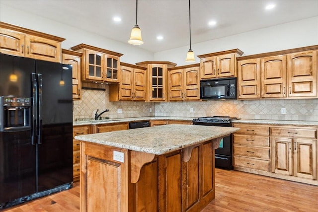 kitchen with hanging light fixtures, black appliances, light hardwood / wood-style floors, light stone countertops, and a kitchen island