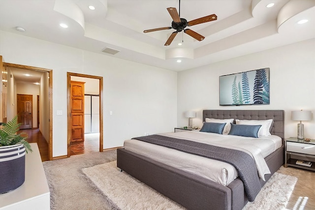 carpeted bedroom with ceiling fan and a tray ceiling