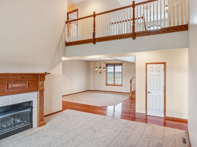 unfurnished living room featuring a tile fireplace, wood-type flooring, a high ceiling, and a notable chandelier