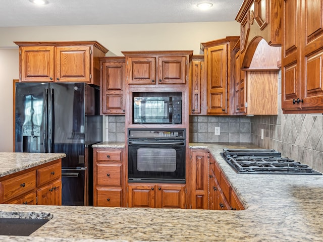 kitchen with backsplash, light stone counters, and black appliances