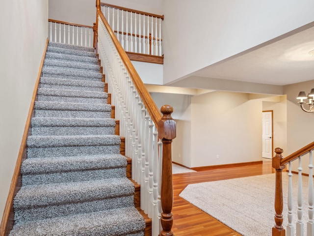 stairs with a high ceiling, a notable chandelier, and hardwood / wood-style flooring