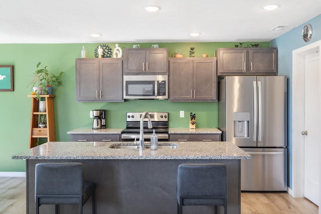 kitchen featuring sink, stainless steel appliances, light stone counters, and an island with sink