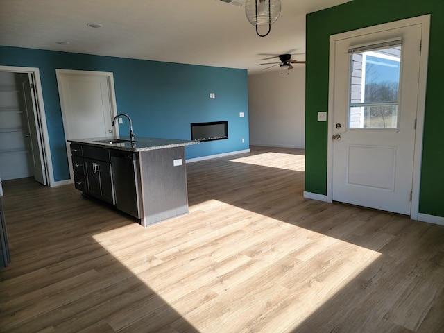 kitchen featuring light wood-type flooring, ceiling fan, a kitchen island with sink, sink, and black dishwasher