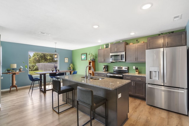 kitchen with sink, a kitchen breakfast bar, light stone counters, an island with sink, and appliances with stainless steel finishes