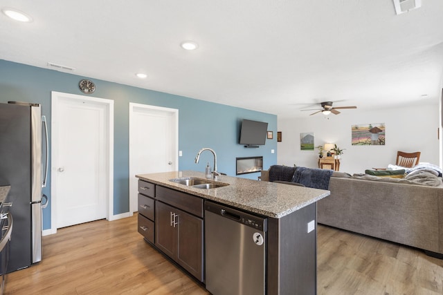 kitchen with dark brown cabinetry, sink, stainless steel appliances, an island with sink, and light wood-type flooring