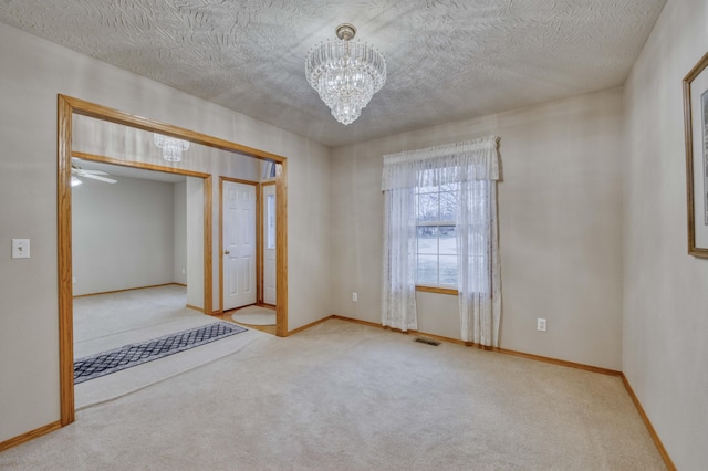 carpeted spare room featuring ceiling fan with notable chandelier and a textured ceiling