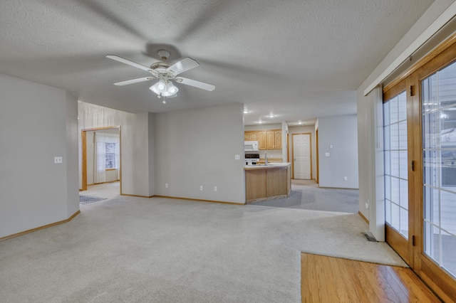 unfurnished living room featuring ceiling fan, french doors, sink, light colored carpet, and a textured ceiling