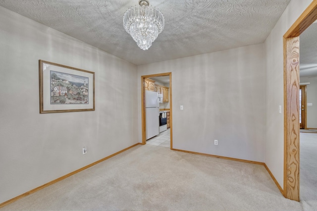 spare room featuring light carpet, a textured ceiling, and a notable chandelier