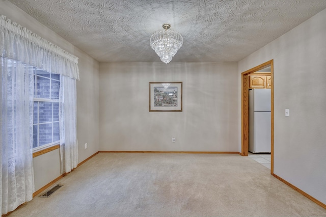 spare room featuring light colored carpet, a textured ceiling, and an inviting chandelier