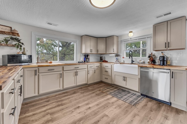 kitchen featuring sink, light wood-type flooring, a textured ceiling, butcher block counters, and stainless steel appliances