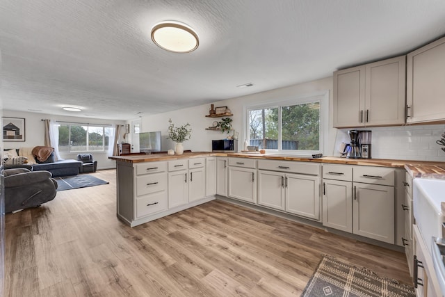 kitchen featuring wood counters, light hardwood / wood-style flooring, backsplash, kitchen peninsula, and a textured ceiling