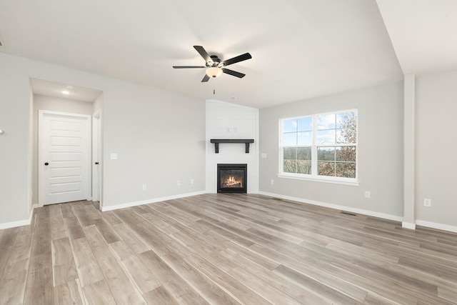 unfurnished living room featuring ceiling fan, a fireplace, vaulted ceiling, and light hardwood / wood-style flooring