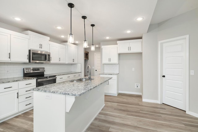 kitchen featuring stainless steel appliances, sink, decorative light fixtures, white cabinetry, and an island with sink