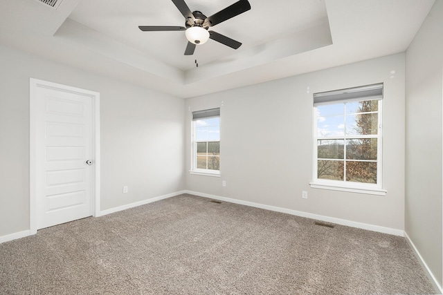 empty room featuring a raised ceiling, ceiling fan, and carpet