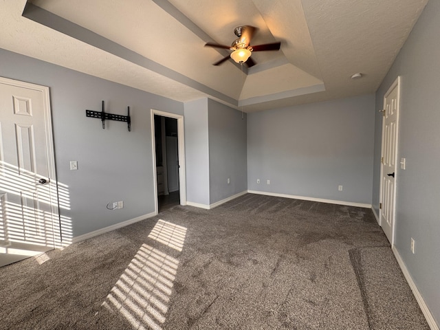 empty room with a tray ceiling, ceiling fan, dark carpet, and a textured ceiling