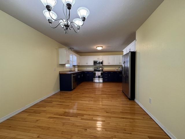 kitchen featuring stainless steel appliances, pendant lighting, a notable chandelier, light hardwood / wood-style floors, and white cabinetry