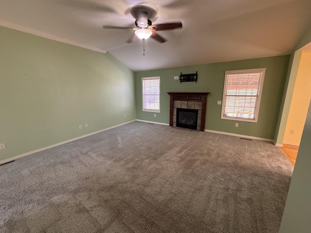 unfurnished living room with ornamental molding, light colored carpet, vaulted ceiling, ceiling fan, and a tile fireplace